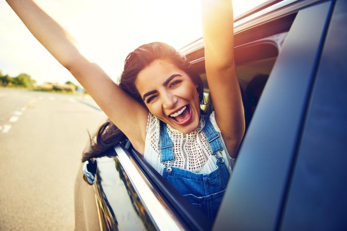 Happy woman with arms outstretched outside of car window