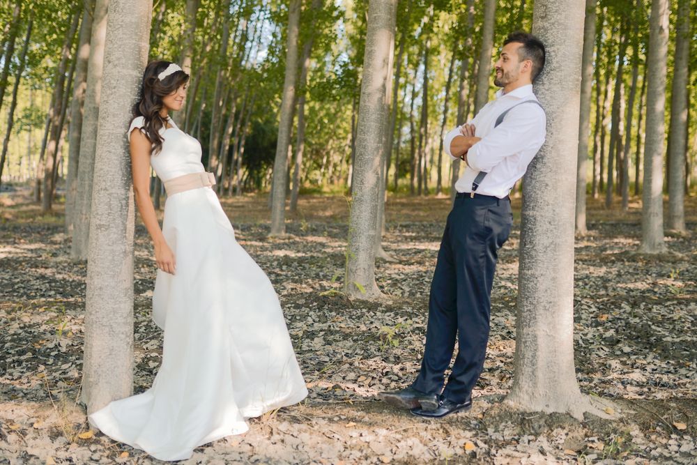Newlywed man and woman facing each other while leaning on trees
