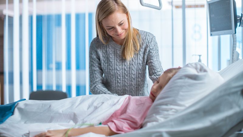 Cute Little Girl Sleeps on a Bed in the Children's Hospital, Caring Mother Covers Her with a Blanket and Caresses Her Forehead