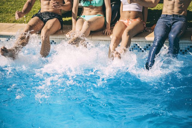 Friends sitting on poolside and splashing with their feet