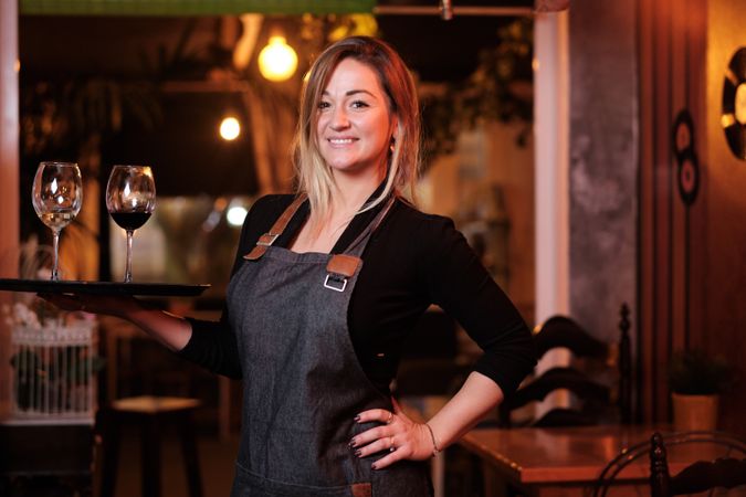 Cheerful waitress holding tray with wineglasses