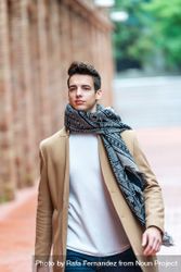 Portrait of confident young man with camel coat and scarf walking down road 5pgW6A
