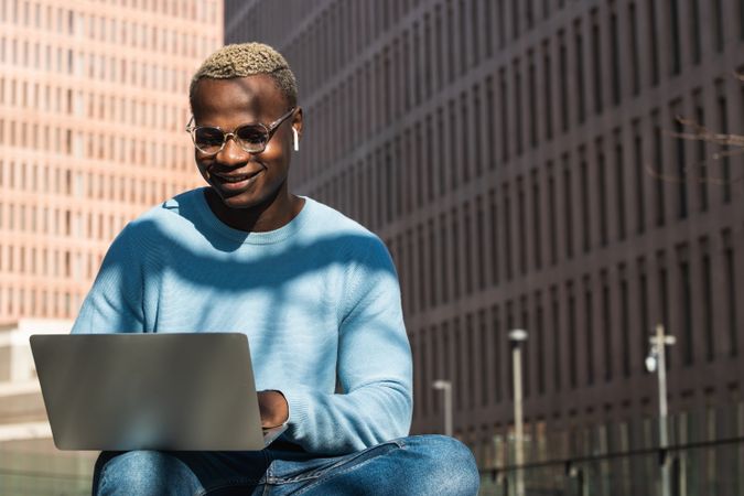 Stylish young Black man working remotely on laptop in city park