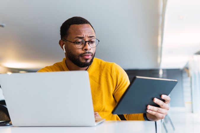 Man with earbuds using tablet and laptop at table