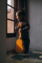 Pondering girl with ukulele looking out window in house
