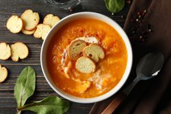 Top view of bowl of delicious pumpkin soup on wooden table, close up