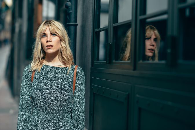 Blonde female wearing casual clothes standing next to windows outside, copy space