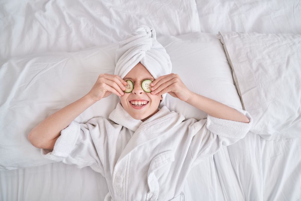 Boy putting cucumber slices on eyes in bedroom