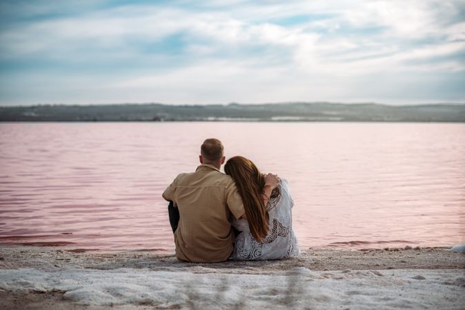 adorable couple sitting on an amazing beach with pink water