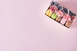 Box of macarons and flowers on pink background