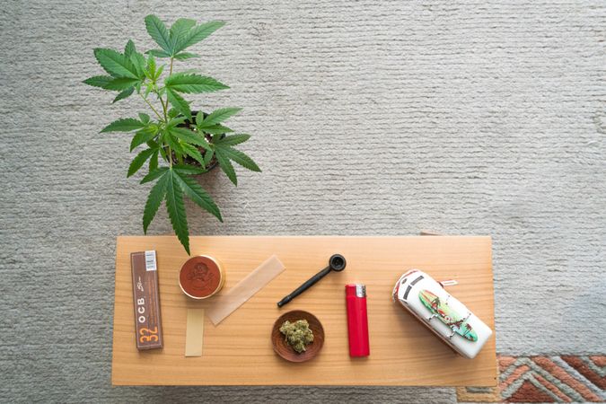 Wooden desk of rolling papers, dried weed, pipe, toy car and plant
