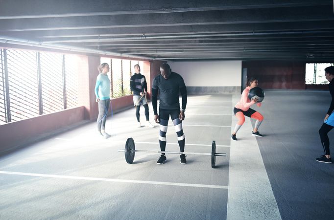 Man standing behind barbell with other people working out around him