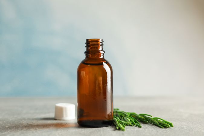 Rosemary oil and leaves on grey table, space for text