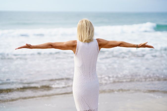 Rear view of older woman with outstretched arms on the coast