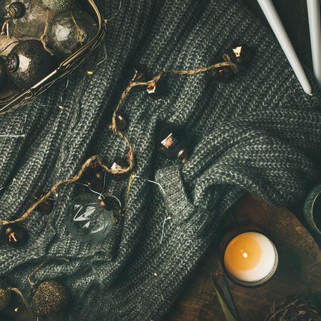 Festive decorations, candles and garland resting on grey woolen sweater, square crop