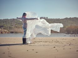 Girl caught up in plastic sheet standing on sandy shore