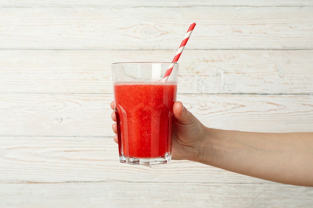 Female hand holds glass of strawberry cocktail on wooden background