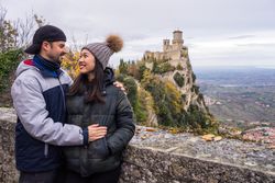Lovely cheerful multiracial couple bonding near by stony fence viewing on castle on hill