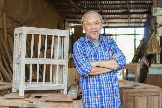 Portrait of mature Asian carpenter with arms crossed at carpentry workshop