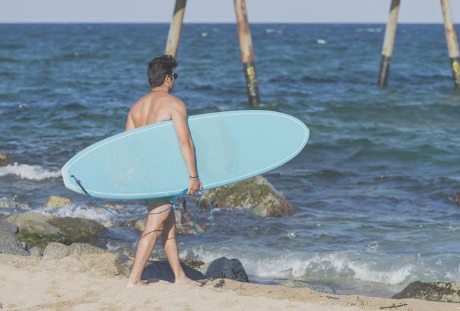 Male surfer holding surfboard approaching the water