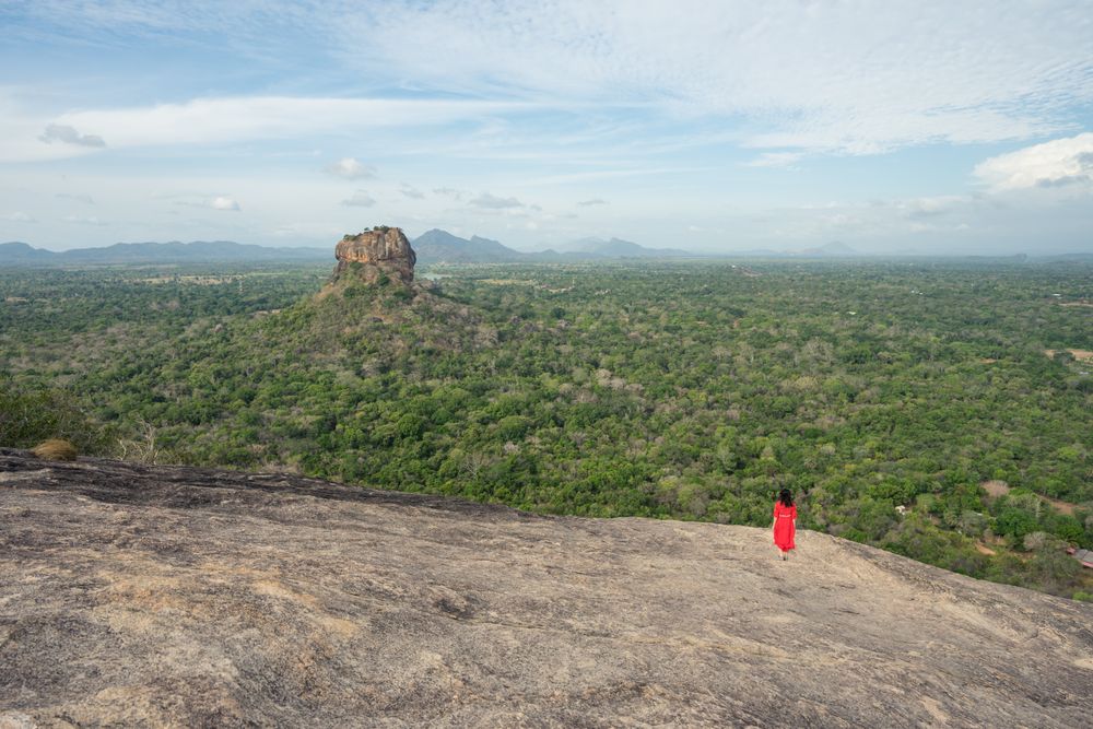 Tourist against solitary rock in middle of green forested plain under clear sky in summer