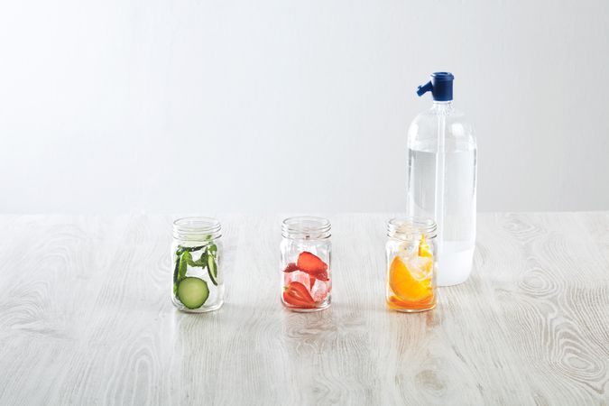 Three mason jars of infused water with distilled water bottle