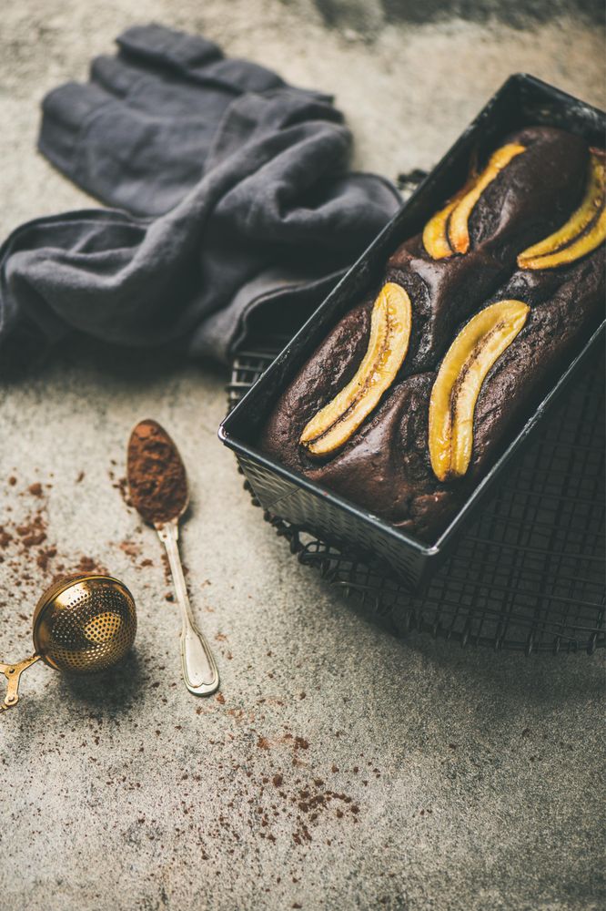Freshly baked dark chocolate banana bread cake on concrete counter, with cocoa powder