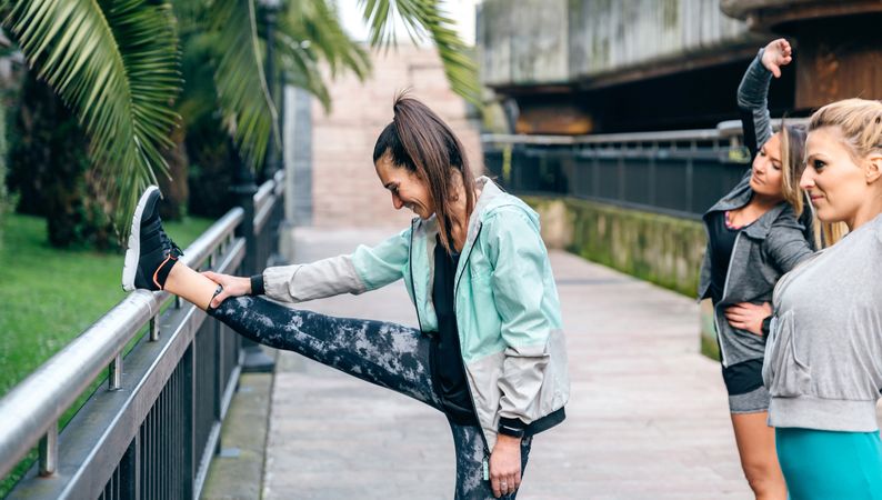Three women runners stretching before training in town