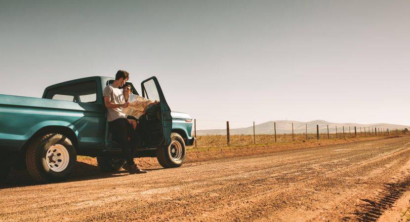 Low angle of man and woman sitting and leaning on vintage truck parked on dirt road