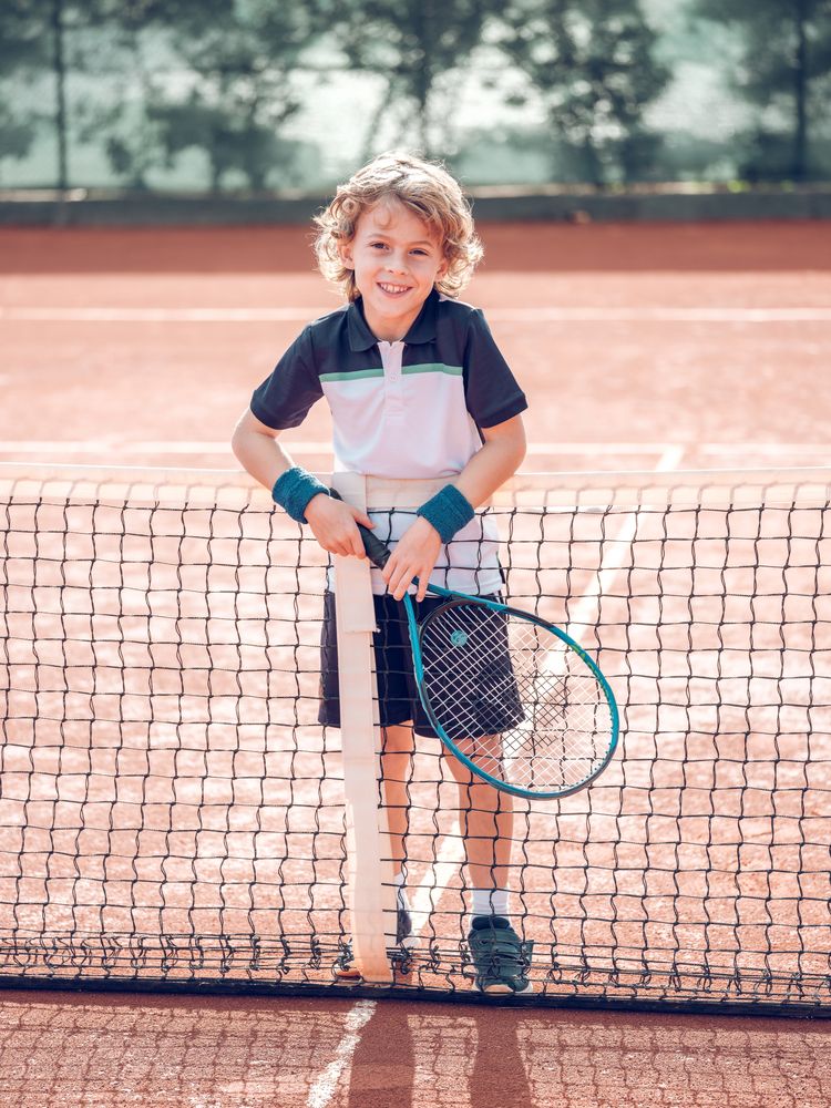 Smiling kid standing near net on court after playing tennis