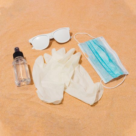 Sunglasses, protective gloves, face mask, hand sanitizer in the sand