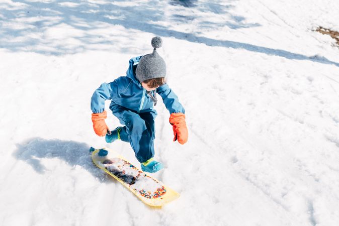 Kid jumping on board riding down snowy mountain