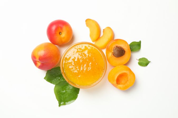 Glass bowl with jam and apricots on blank background, top view