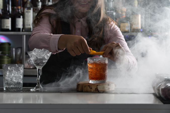 Bartender squeezing orange peel over a cocktail