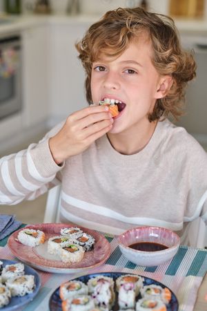 Little boy eating delicious sushi in kitchen