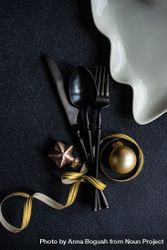 Dark cutlery on dark background tied with festive gold ribbon, and baubles 5p79e0