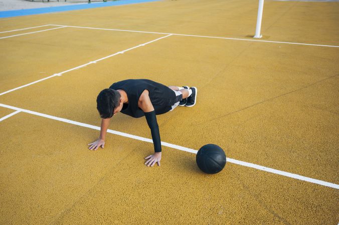 Young man doing push up and playing on basketball court outdoor.