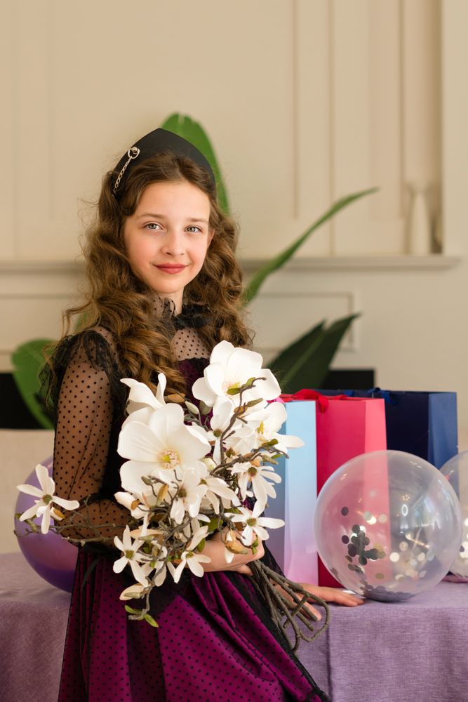Girl holding flowers and balloons at birthday celebration.