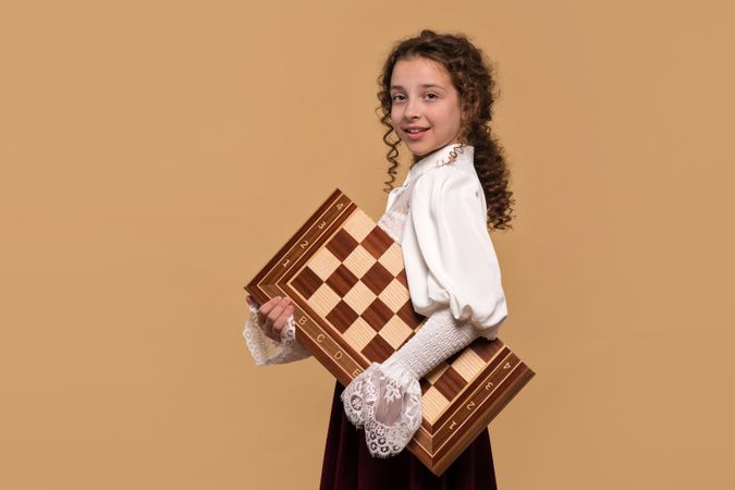 Young girl holding large chessboard under her arm