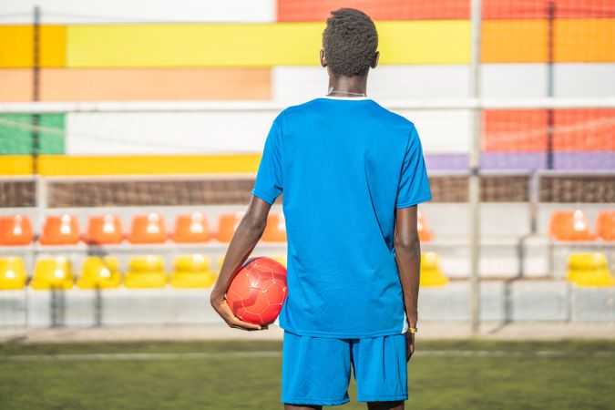 Black football player with ball standing on stadium