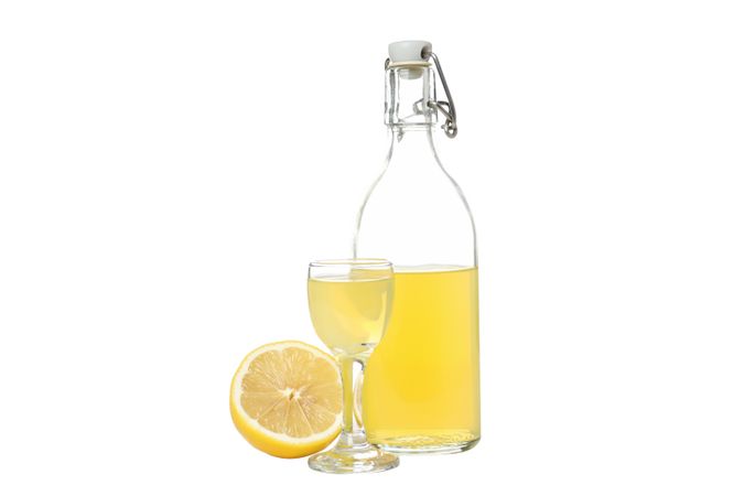 Half of lemon, bottle and glass with limoncello, isolated on light background