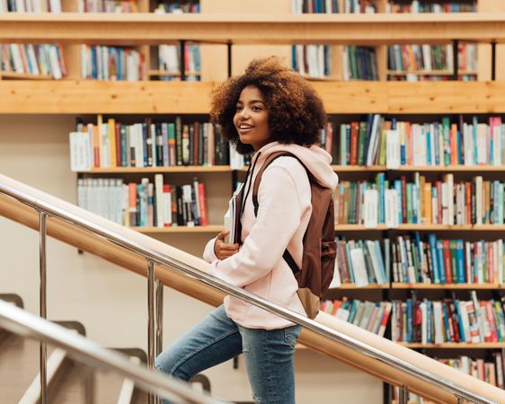Curly haired young woman walking up library stairs