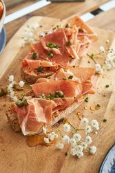 Delicious bruschettas with prosciutto and capers served on wooden board