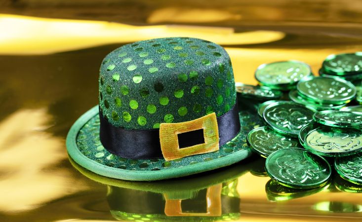 Saint Patrick celebration with coins and hat on gold background setting