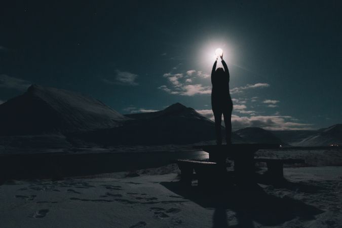 Woman on table on coast near water at night with moon in sky