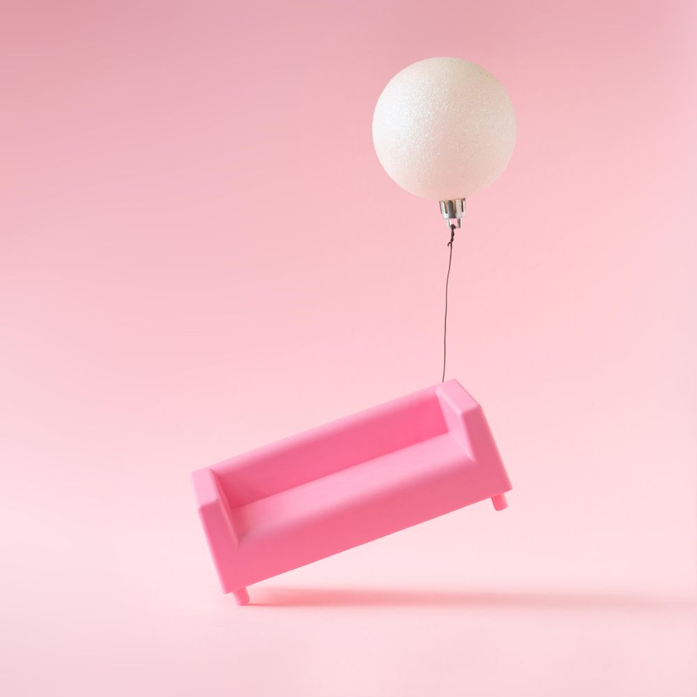 Pink sofa with Christmas bauble decoration on pink background with bauble floating side of sofa