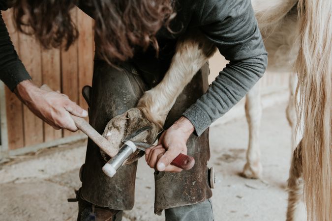 Man shoeing horse near stable