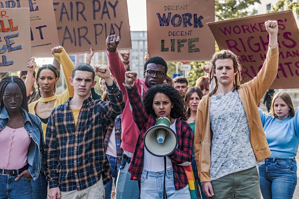 A group of multi-ethnic youth protesting for fair pay and work access, raising fists