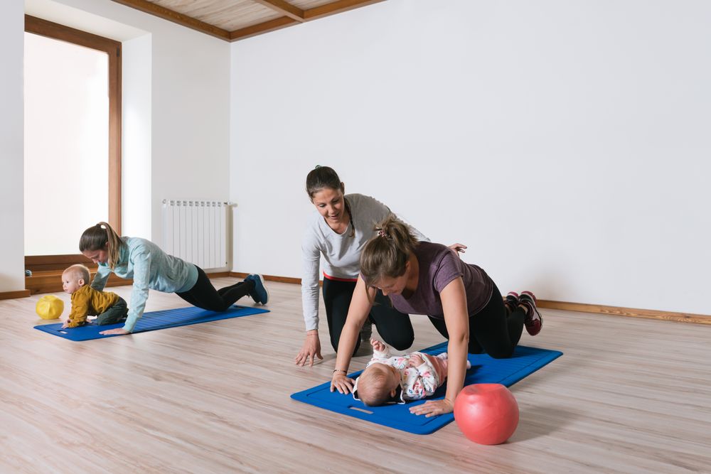 Fitness instructor helping mother with push ups