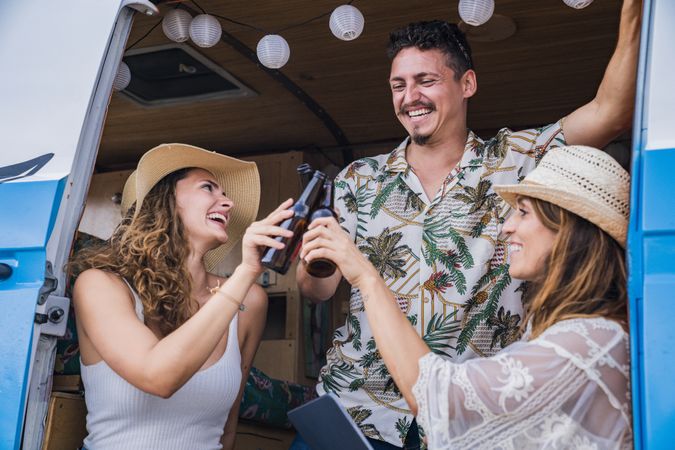Smiling friends clinking bottles of beer celebrating vacation